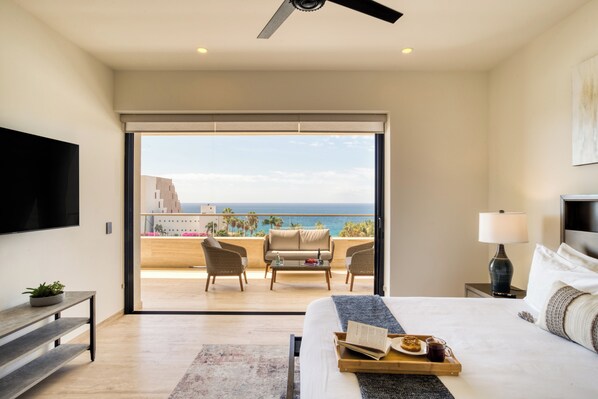 A hotel room with a balcony, a bed, a TV, a lamp, and a tray with a book and a drink. - Marella Cabo (Cabo San Lucas)
