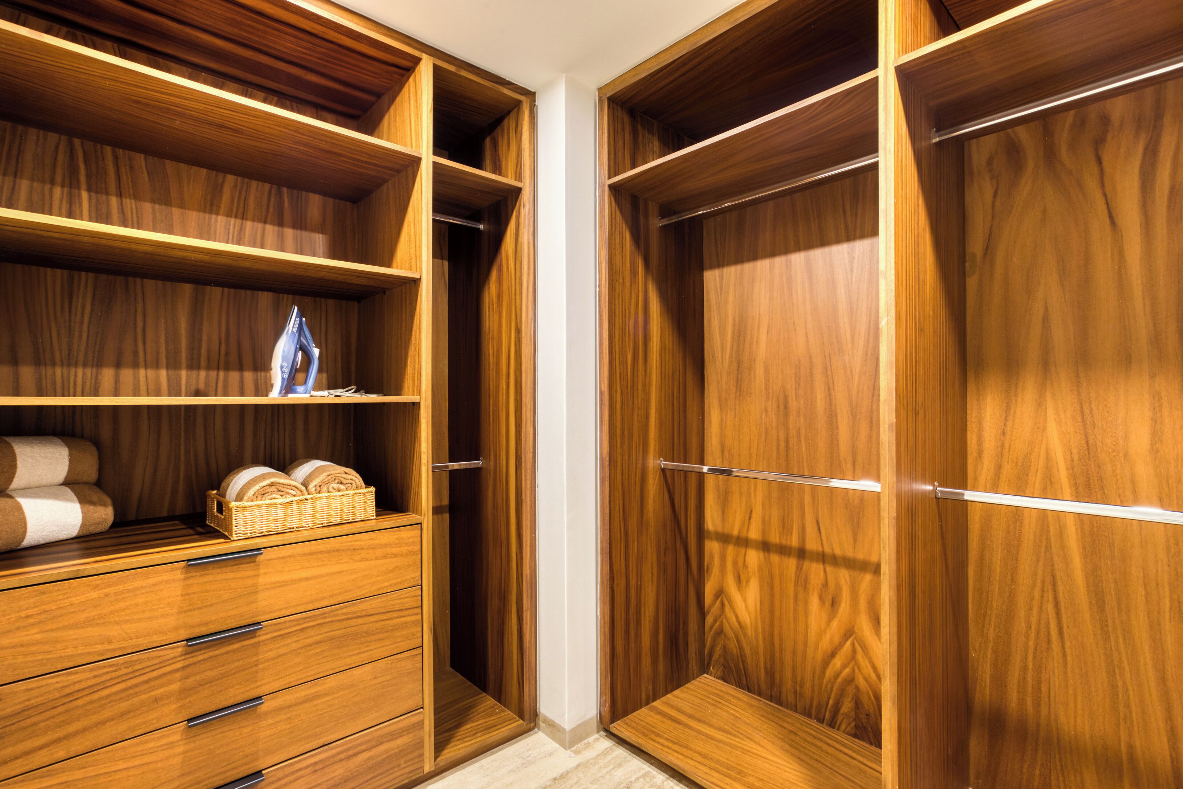 A wooden closet with multiple shelves and drawers, containing neatly rolled towels and a wicker basket.