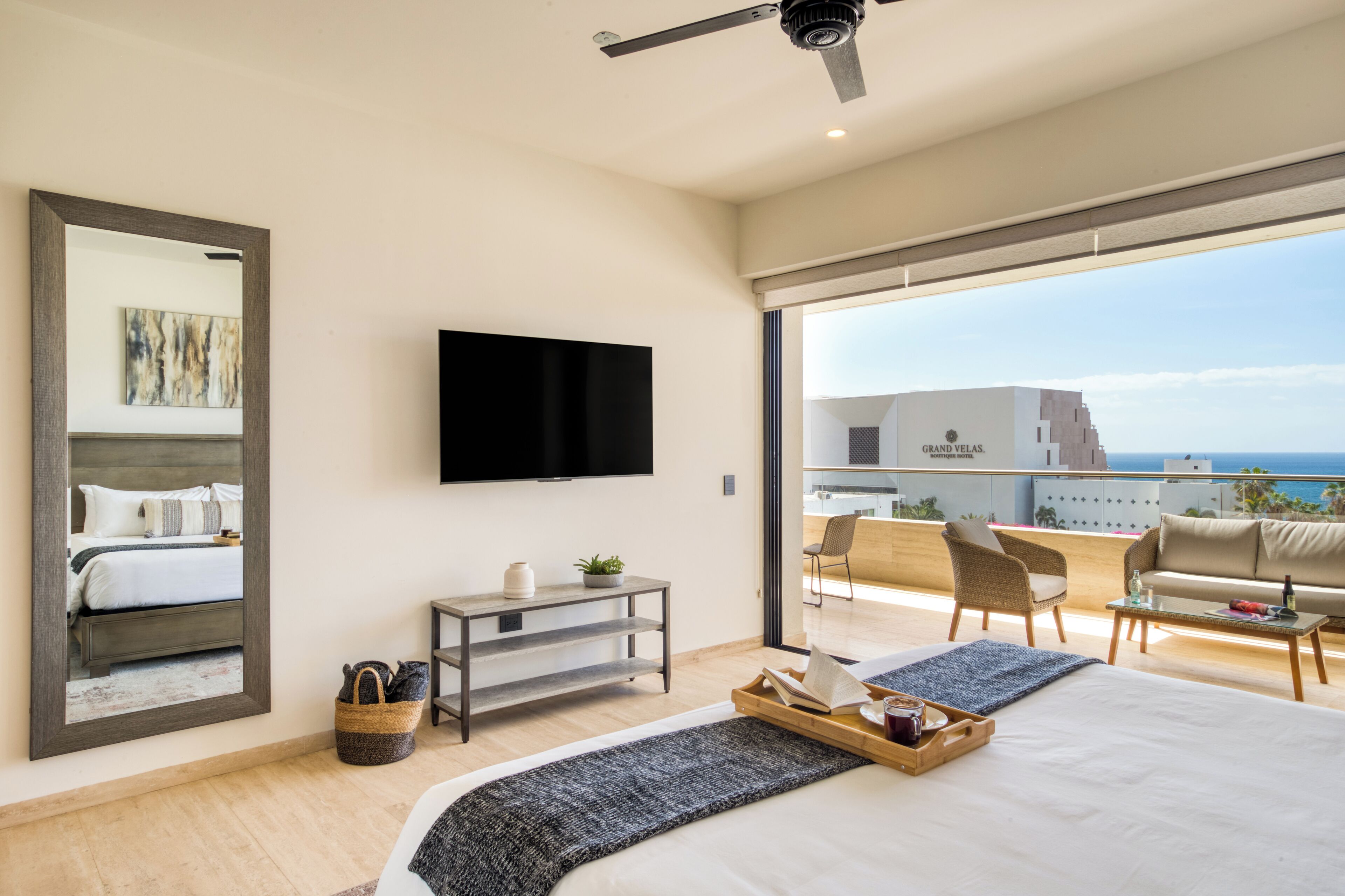 Quarto de hotel moderno com uma cama grande, televisão de tela plana, varanda com vista para o mar e área de jantar.