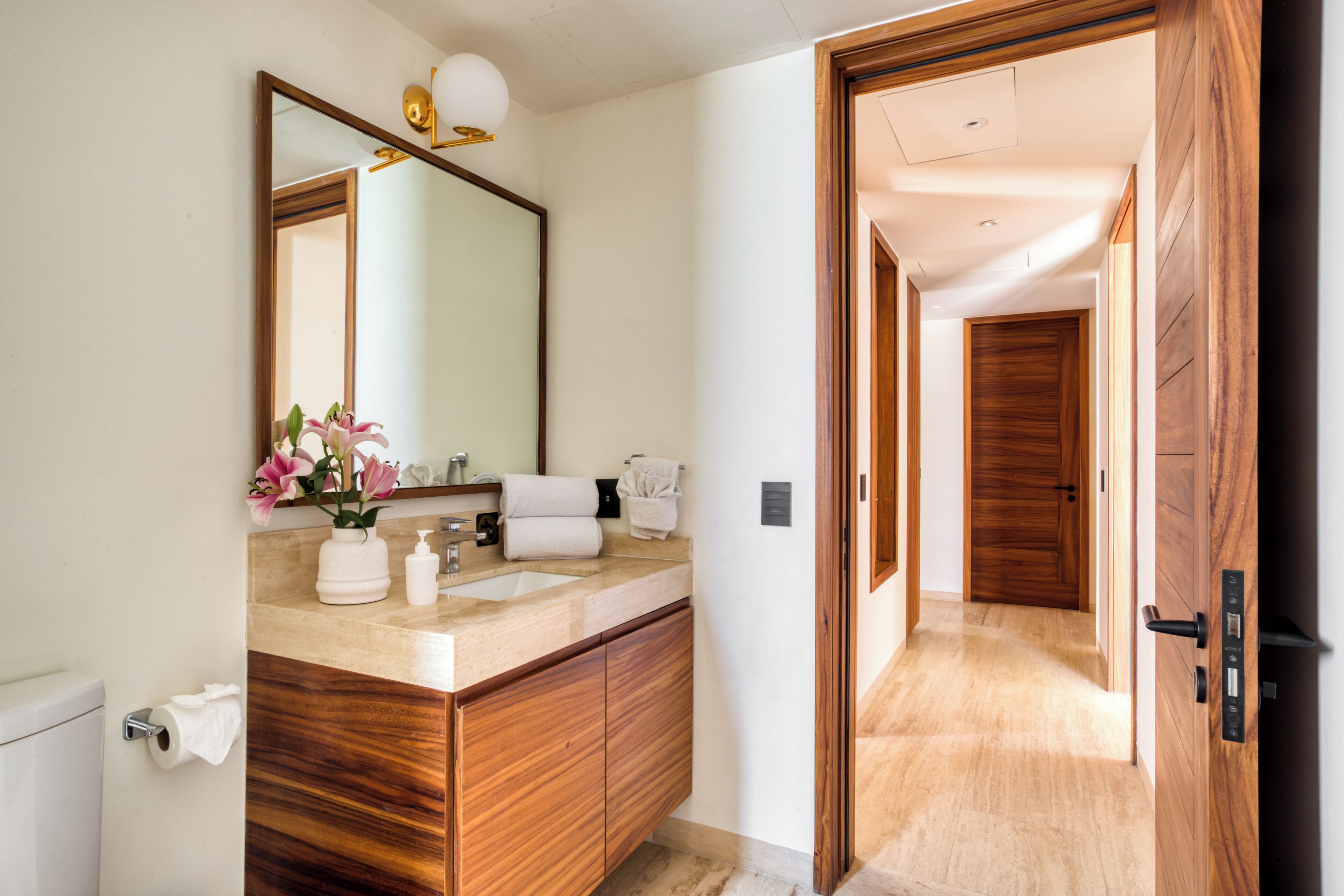 A modern bathroom with a wooden vanity, a large mirror, and a vase of flowers.