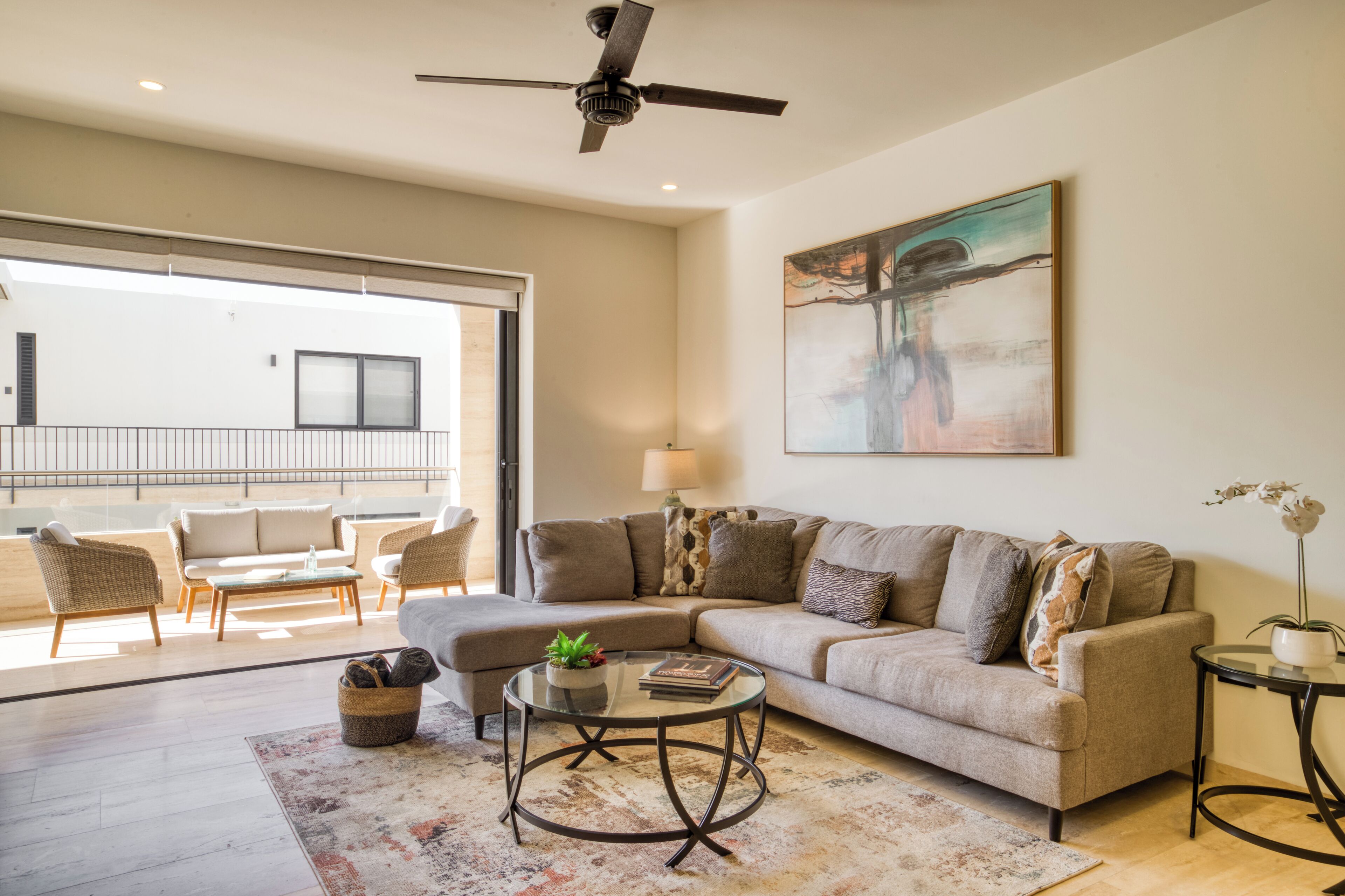 A modern living room with a sectional sofa, a glass coffee table, and a ceiling fan.