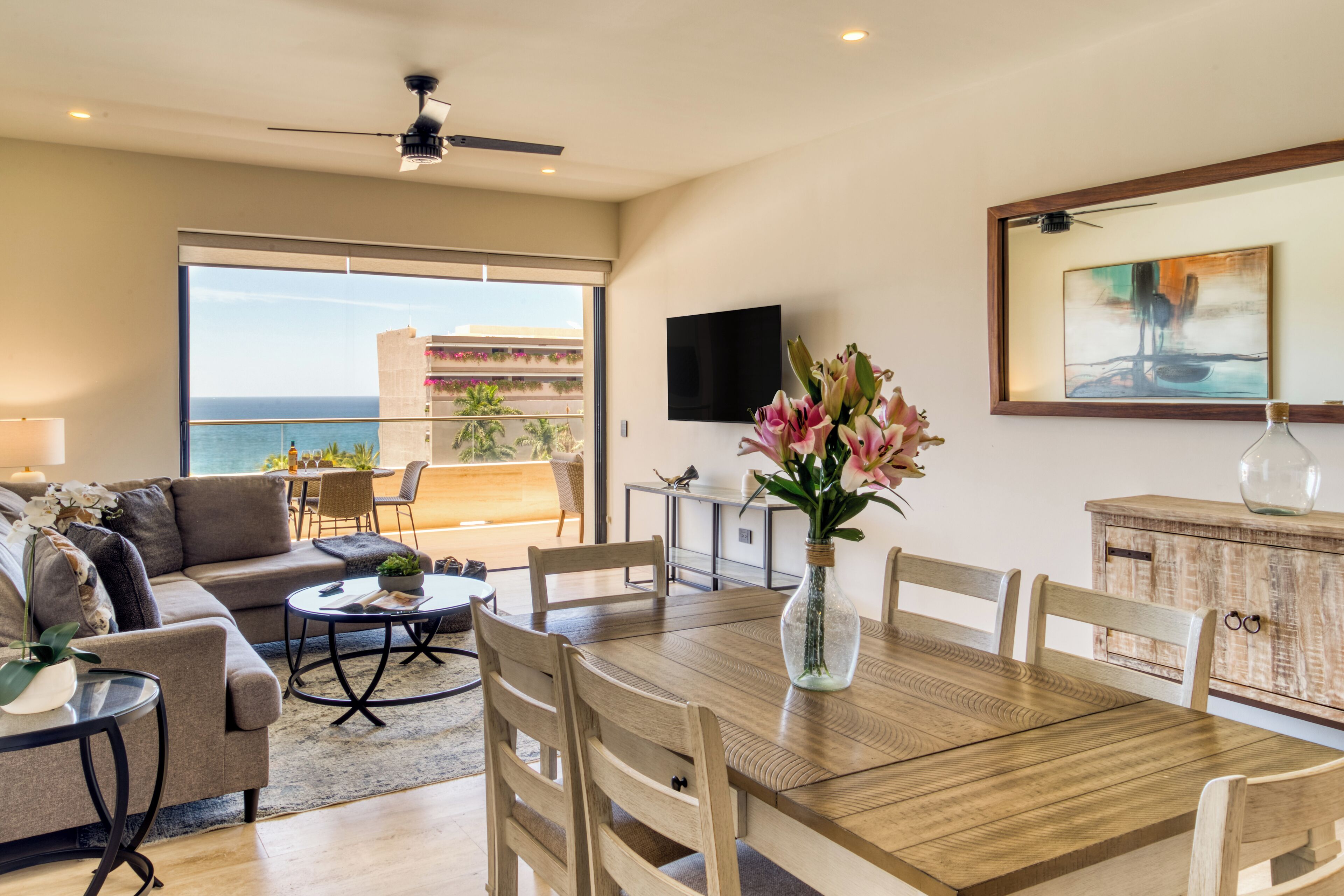 A modern living room with a dining area, large windows, and a view of the ocean.
