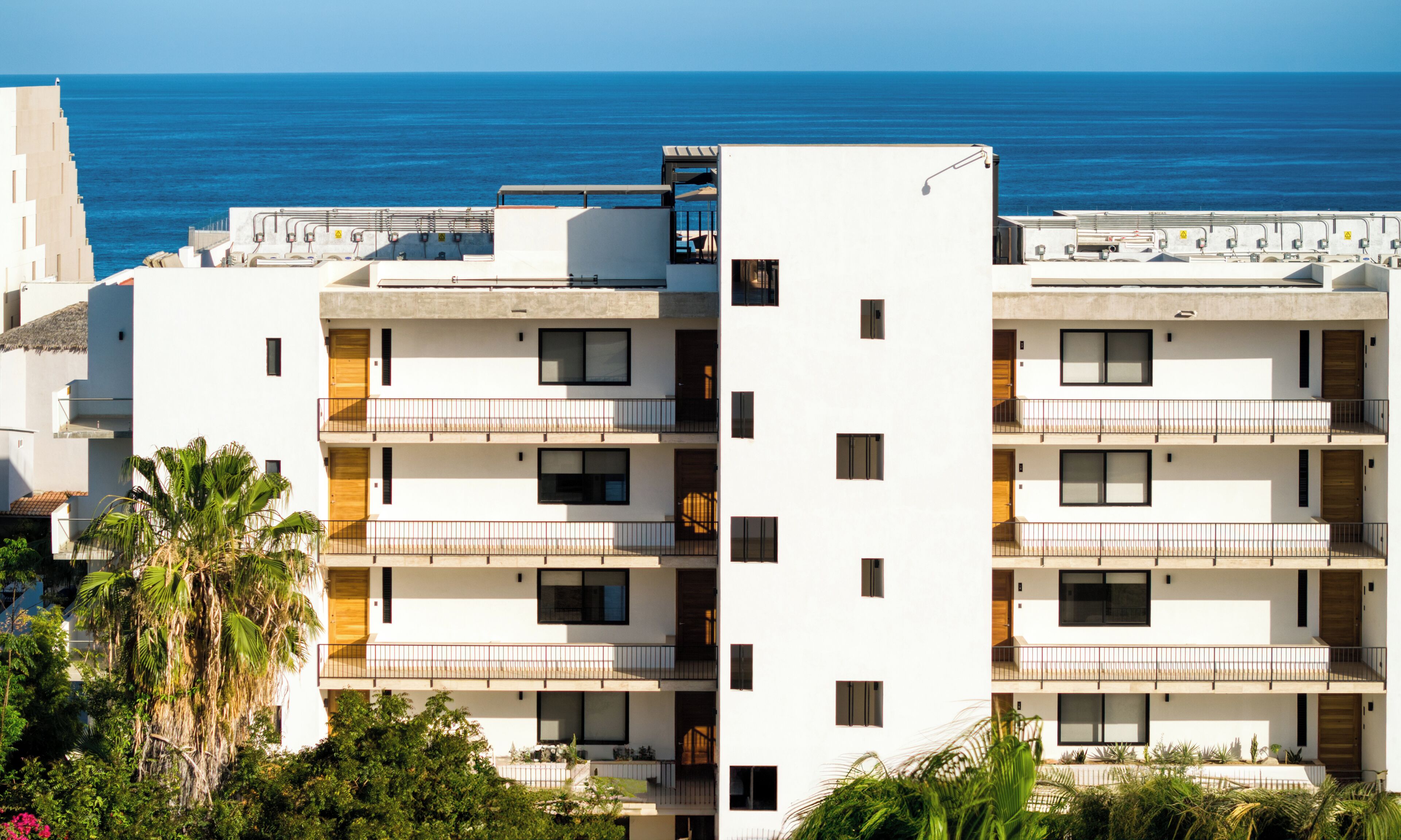Un immeuble moderne à plusieurs étages, doté de balcons, de murs extérieurs blancs et offrant une vue sur la mer.