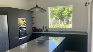 A modern kitchen with a central island, dark cabinetry, and a large window providing a view of greenery outside. - Villa Tropic ' AL (Saint-François)