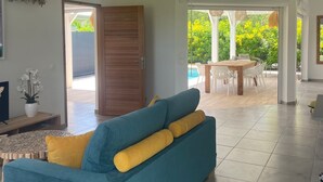 A spacious living area with a blue sofa, wooden door, and a view of an outdoor patio with a pool. - Villa Tropic ' AL (Saint-François)