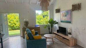 A modern living room with a sofa, TV, and a large window offering a view of greenery. - Villa Tropic ' AL (Saint-François)