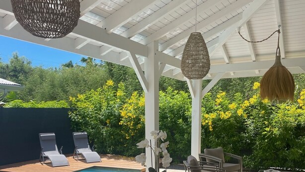 A covered outdoor dining area with a pool, white chairs, and hanging lights. - Villa Tropic ' AL (Saint-François)