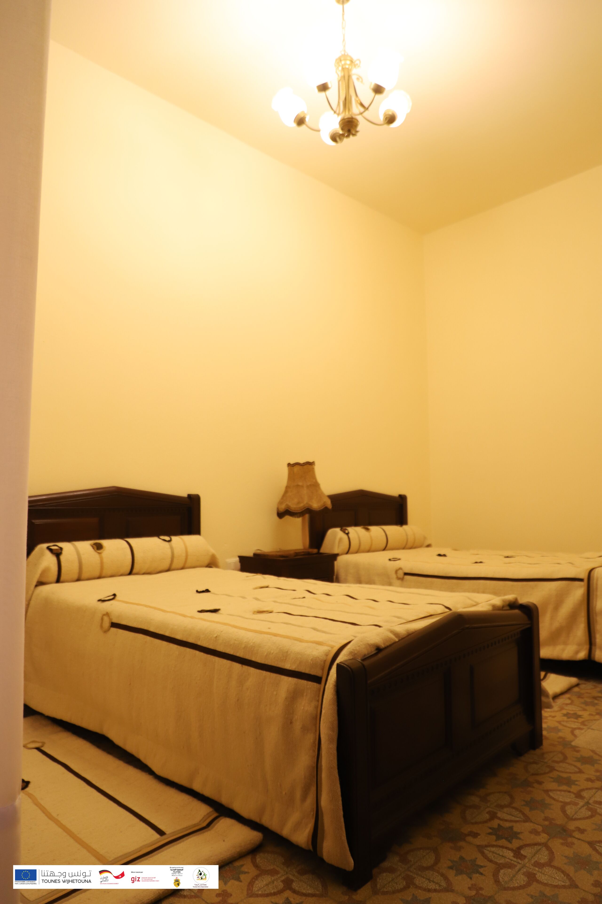 Una camera d'albergo con due letti, un lampadario e una moquette fantasia.