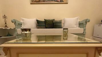 A vintage-style sofa with a glass-top coffee table in a room with a painting on the wall.