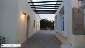A corridor with a wooden pergola, white walls, and a brick floor.