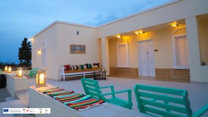 A modern building with a white exterior, a covered patio area with seating, and decorative lighting. - Gîte FEKI (Agareb)