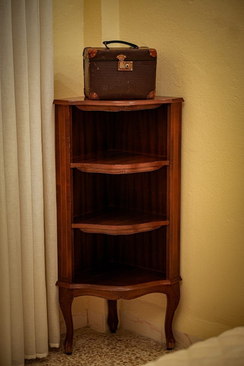 Una estantería de madera con una maleta antigua encima.