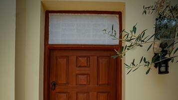 A wooden door with a metal handle and a keyhole, set in a hallway with patterned floor tiles.