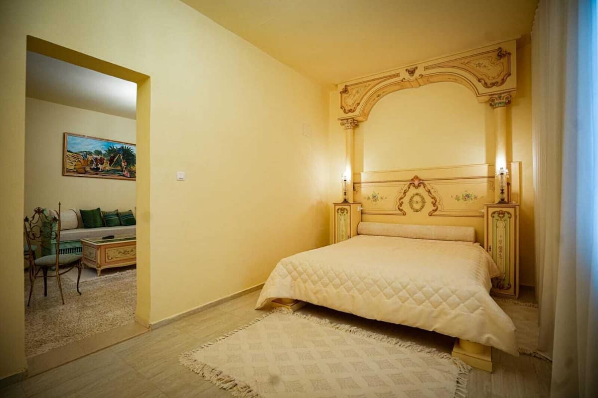 Quarto com uma cama grande, uma mesa de cabeceira, uma cadeira e um quadro na parede.