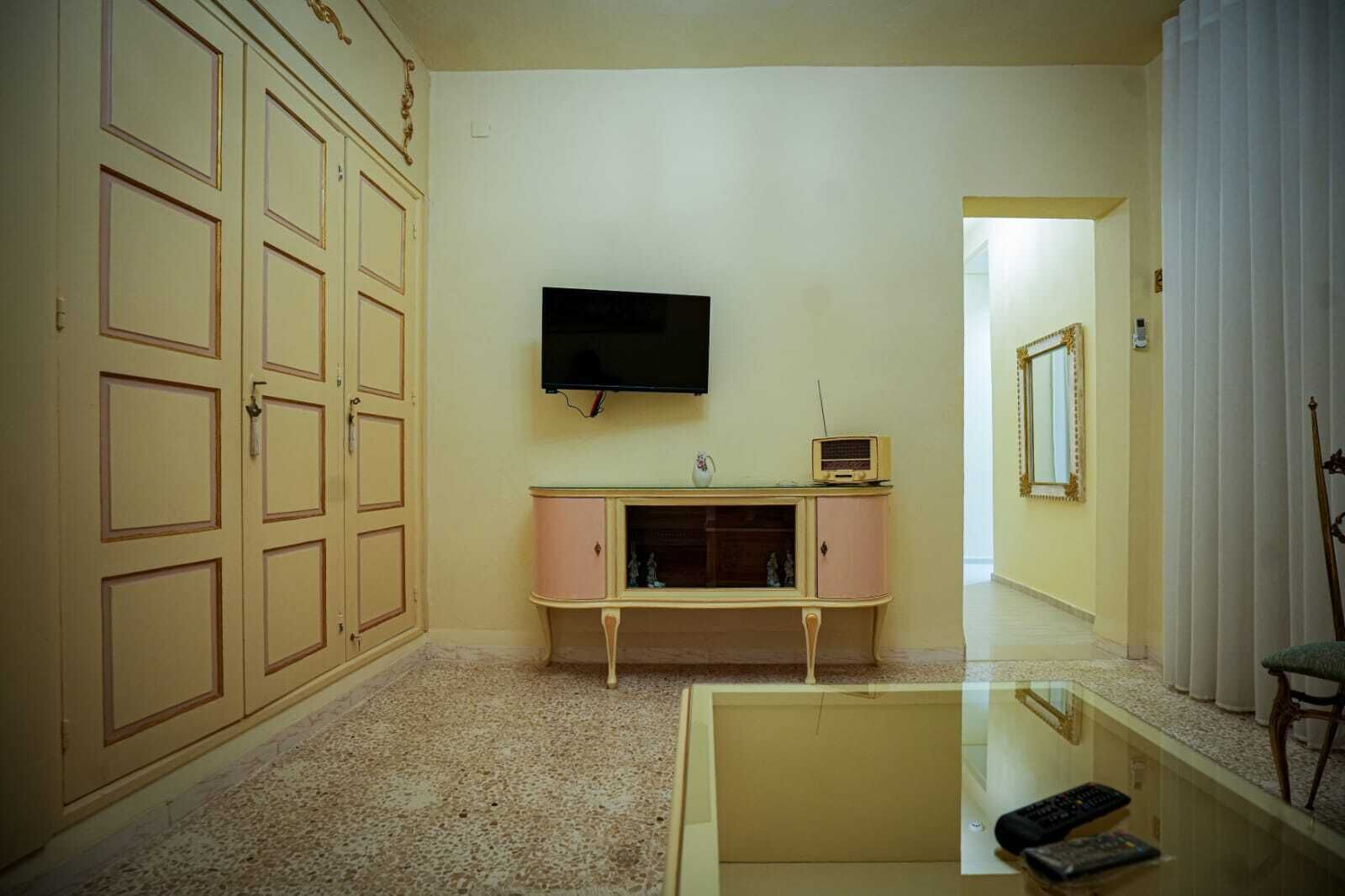 Una sala de estar con televisor, un aparador rosa y una mesa de centro de vidrio.