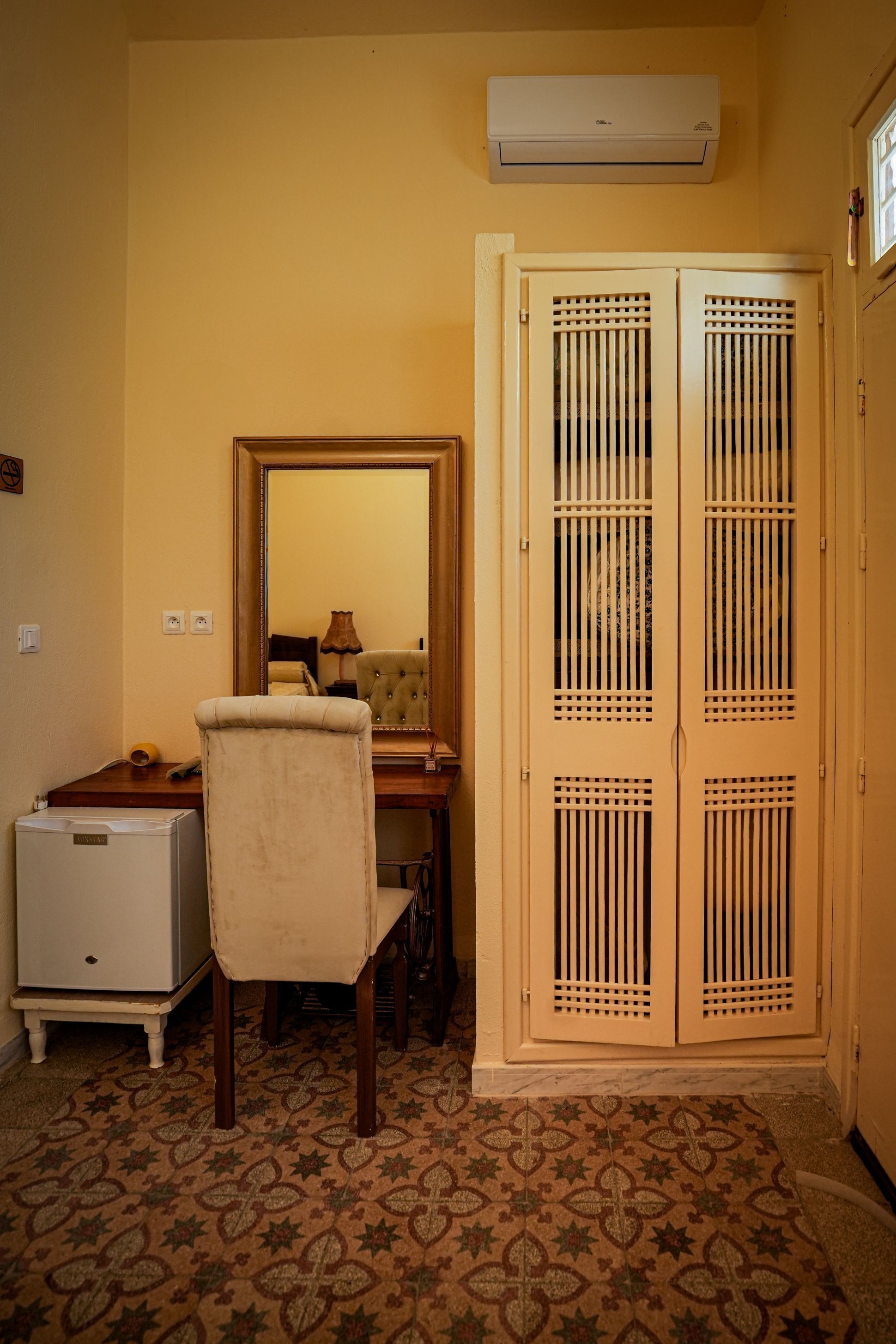 A room with a desk, chair, wardrobe, and a mirror.