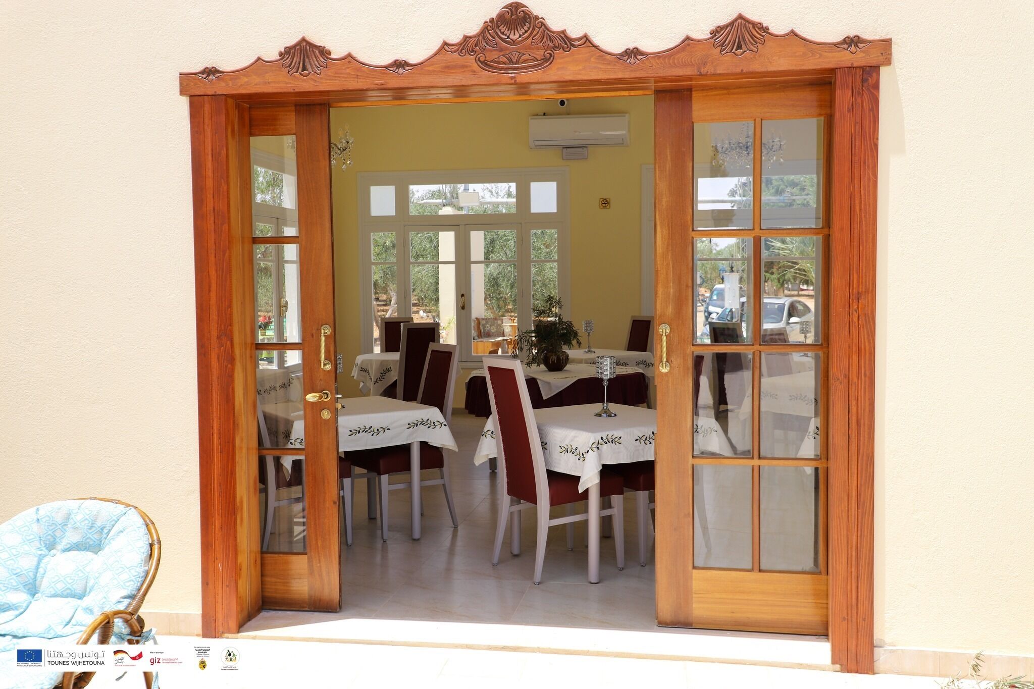 A dining area with a wooden-framed entrance, tables with white tablecloths, and red chairs.