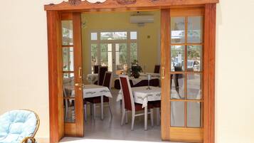 A dining area with a wooden-framed entrance, tables with white tablecloths, and red chairs.