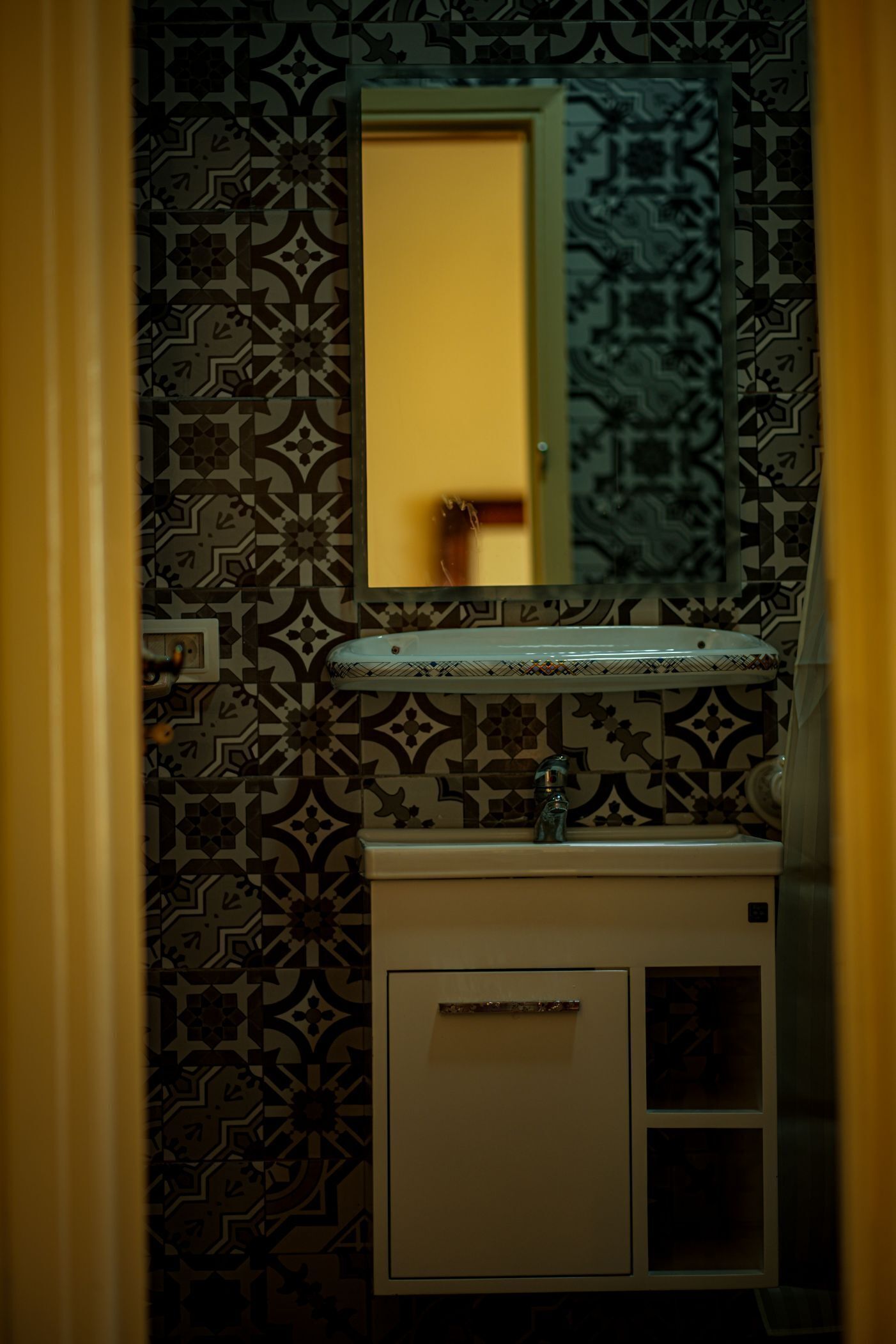 A bathroom with patterned tiles, a sink, and a mirror.