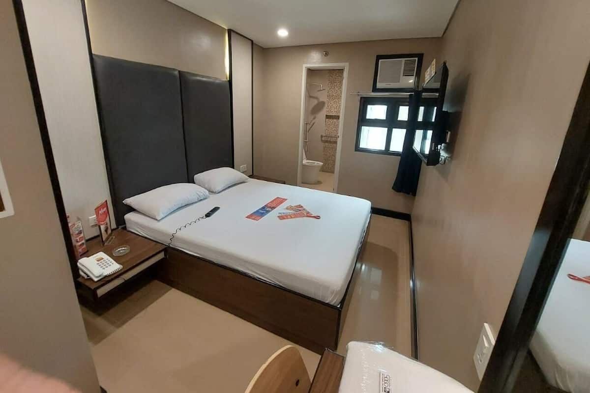 A hotel room with a bed, bedside table, and a TV mounted on the wall.