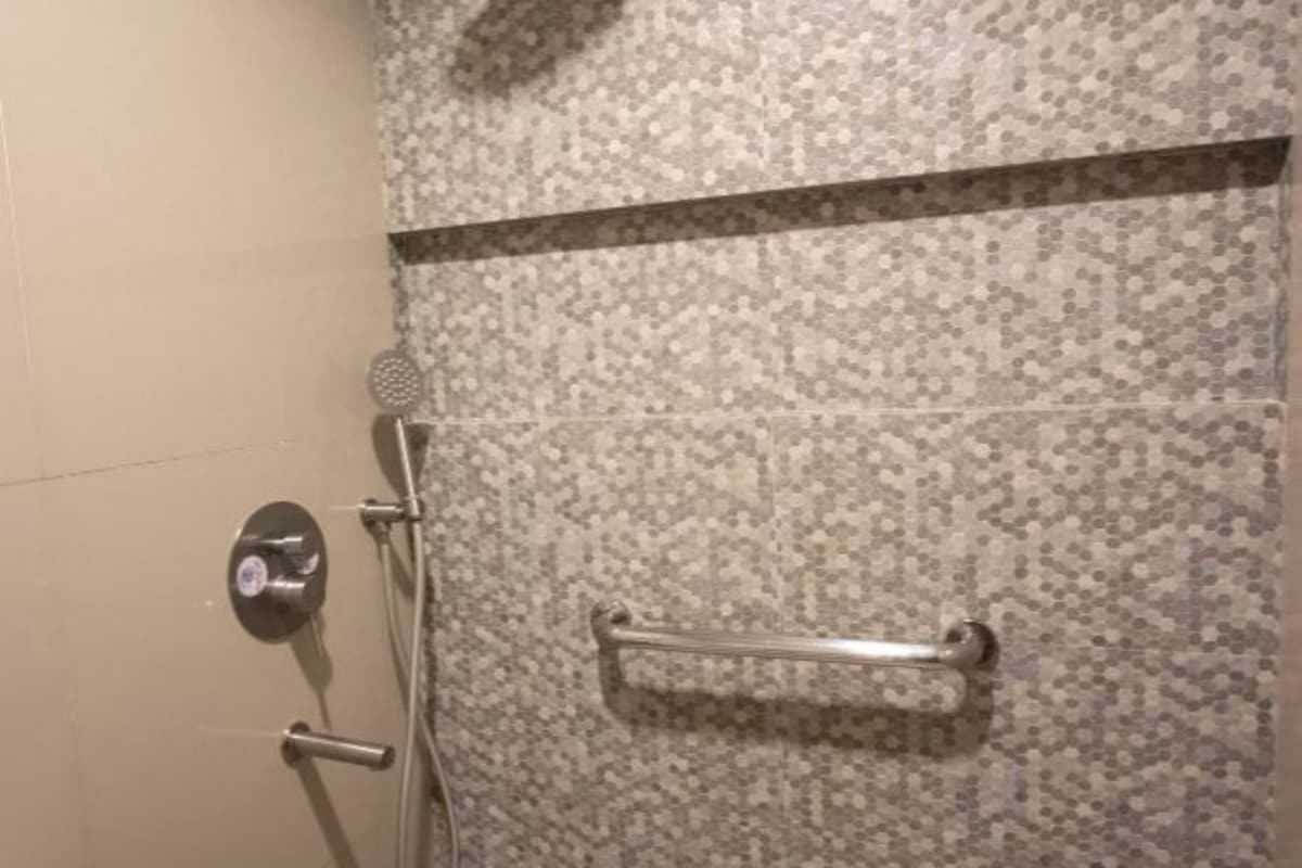 A shower with a tiled wall, a showerhead, and a handrail.