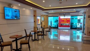 A clean, modern lobby with a reception desk, a digital screen displaying a message, and a few tables and chairs arranged for guests. - Hotel Sogo Timog 2 (Quezon City)