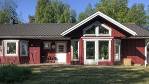 A red wooden house with a sloped roof, large windows, and a front porch.
