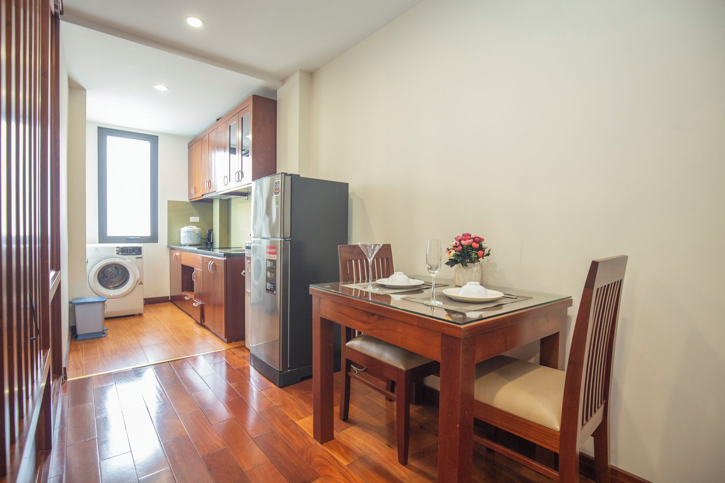 Cozinha compacta com armários de madeira, geladeira e máquina de lavar.