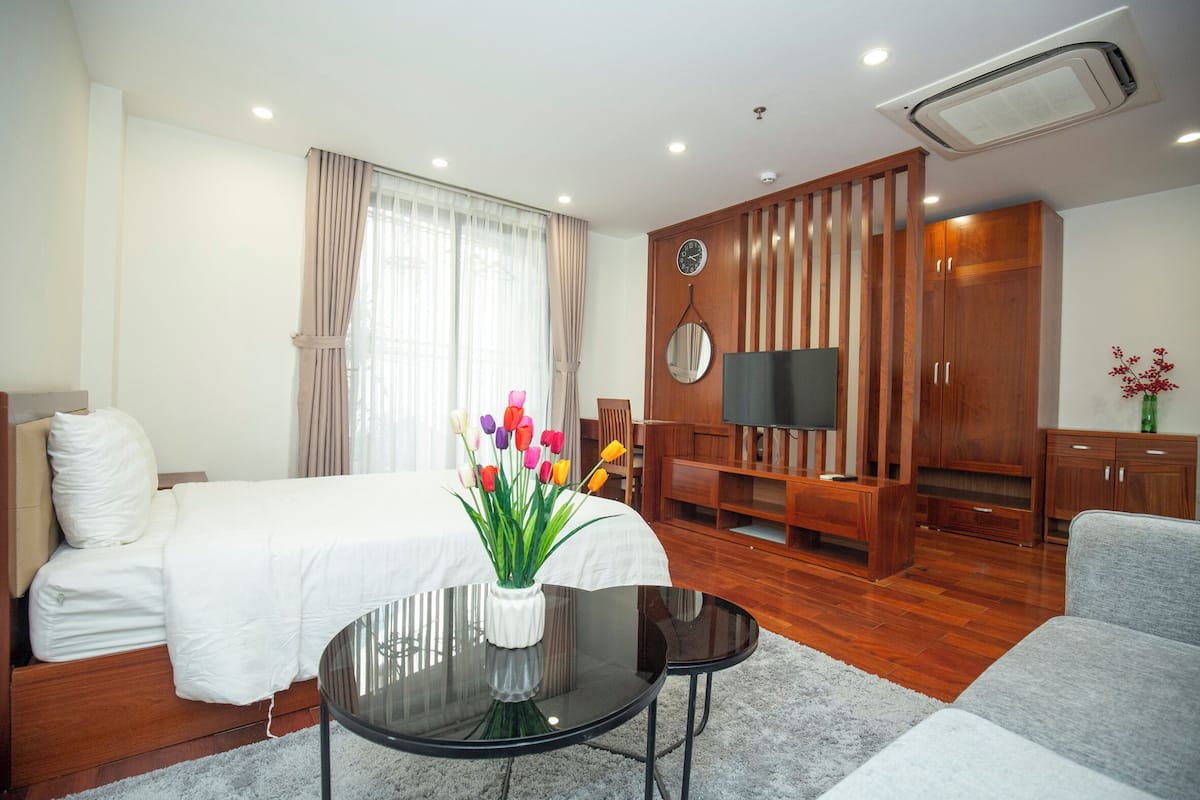 Una habitación de hotel moderna con una cama, una mesita con un florero, un televisor y muebles de madera.