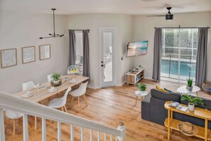 A modern living room with a wooden dining table, white chairs, a grey sofa, and a TV mounted on the wall. - Family home w/ pool & game room near Disney (Davenport)