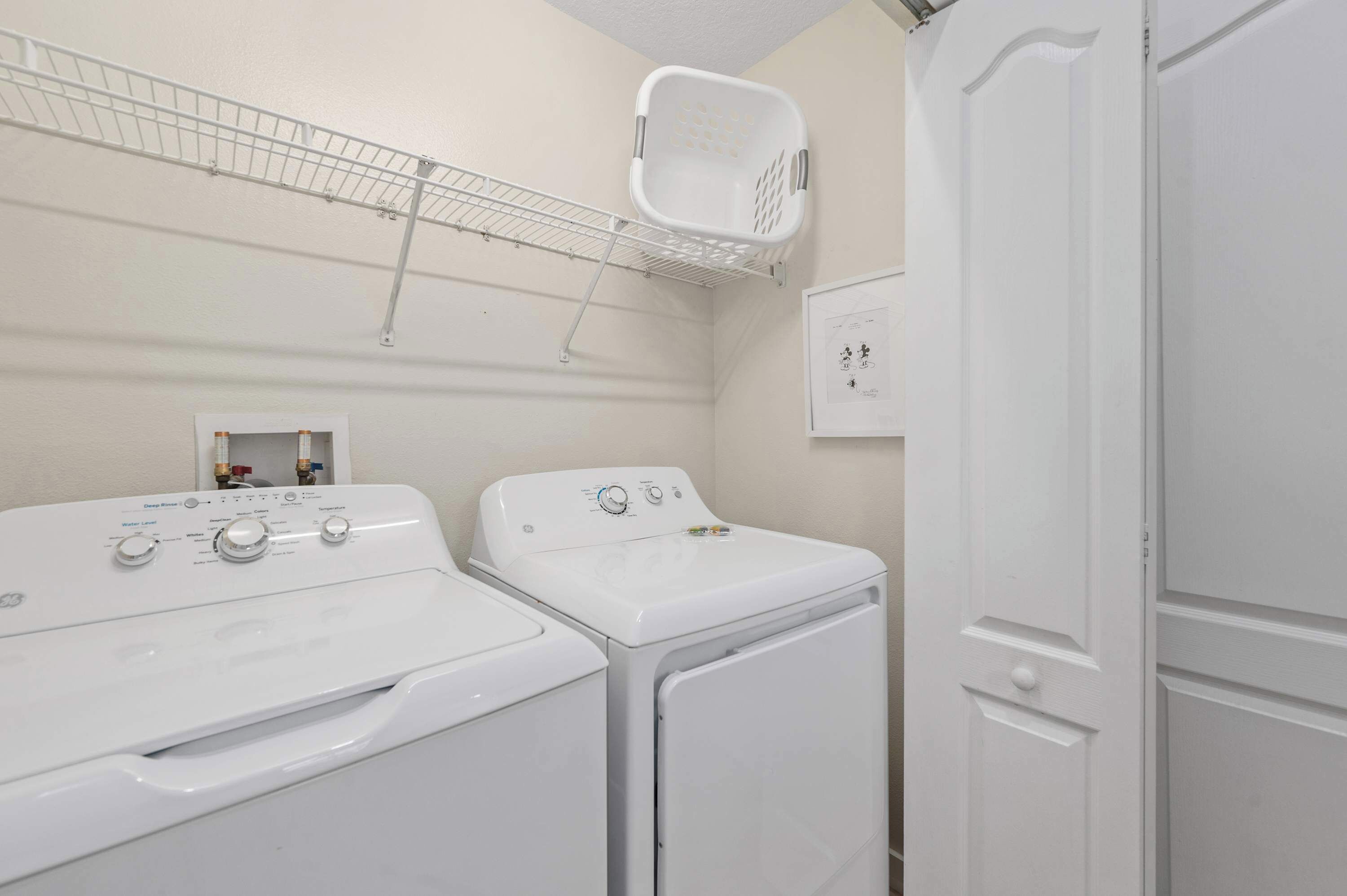 A laundry room with two white washers and dryers, a drying rack, and a utility wall with a water meter.