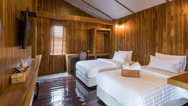 A wooden-paneled room with two beds, a small table, and a TV mounted on the wall. - U Villa Chiangkhan (Chiang Khan)