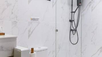 Moderni kylpyhuone, jossa on wc, suihkukaappi ja marmorilaatoilla verhoiltu seinä.