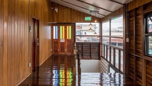 A wooden interior hallway with a wet floor, a visible exit sign, and a view through large windows. - U Villa Chiangkhan (Chiang Khan)