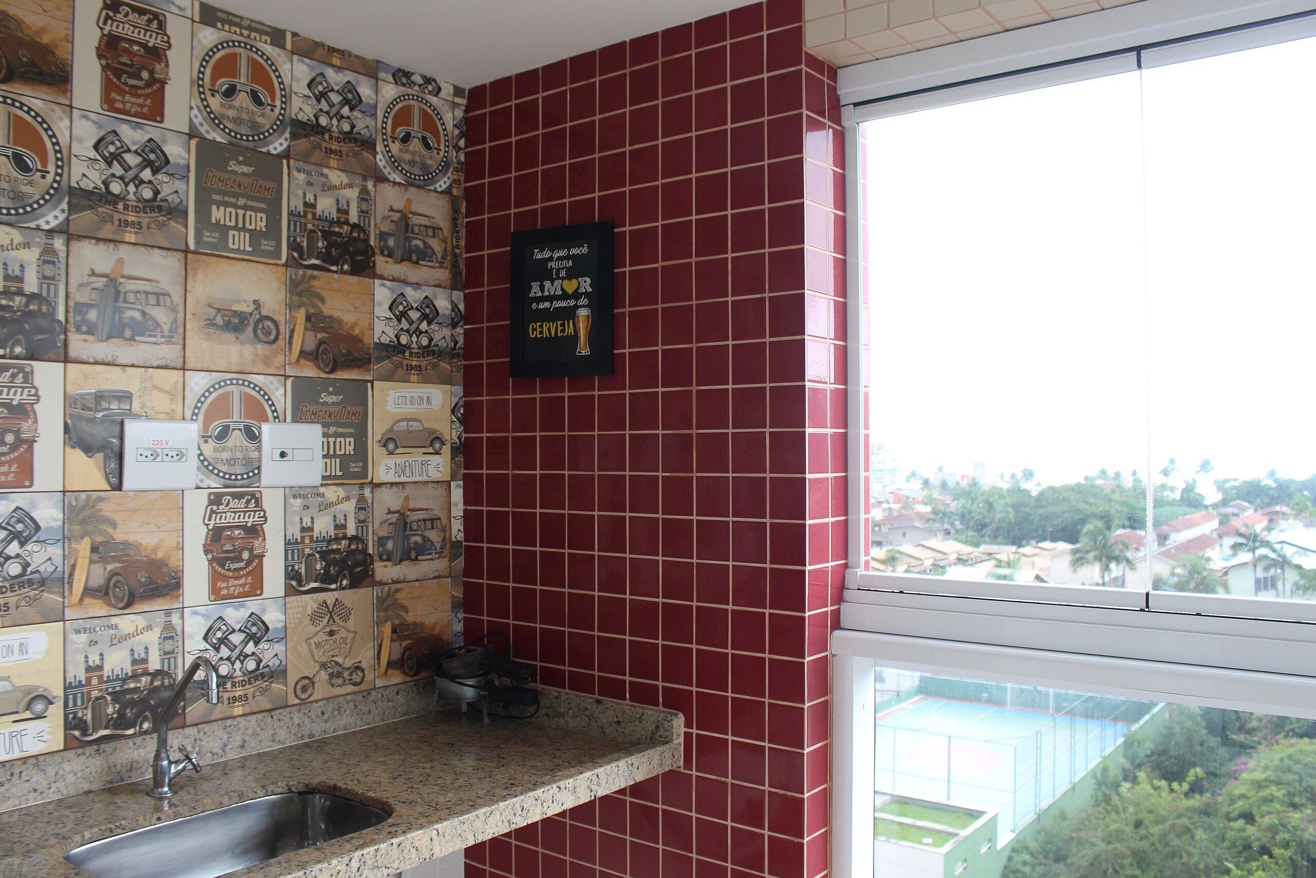 A kitchen with a red tiled backsplash and a window overlooking a residential area.