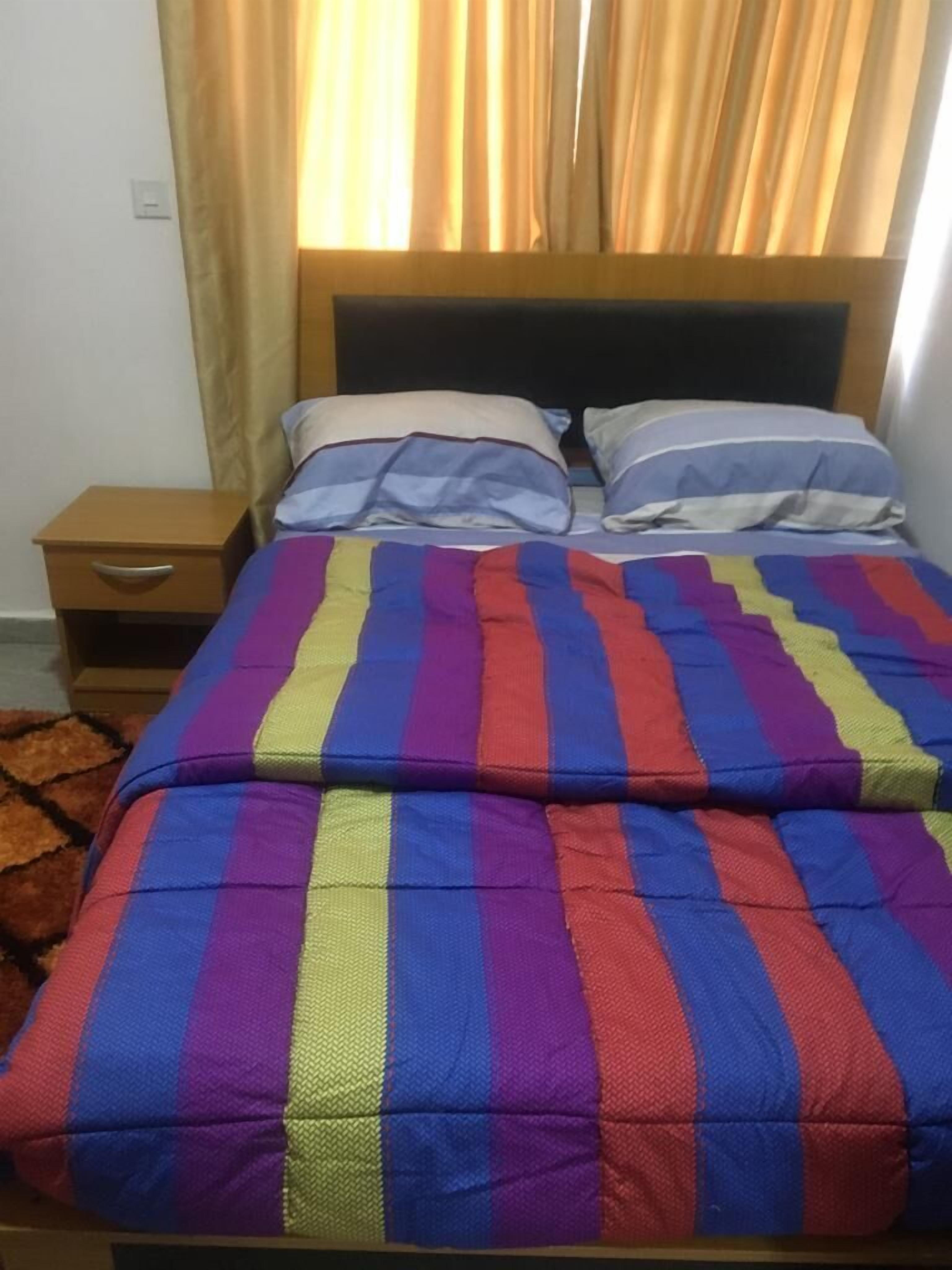 A bed with a colorful striped bedspread, a wooden headboard, and a nightstand with a drawer.