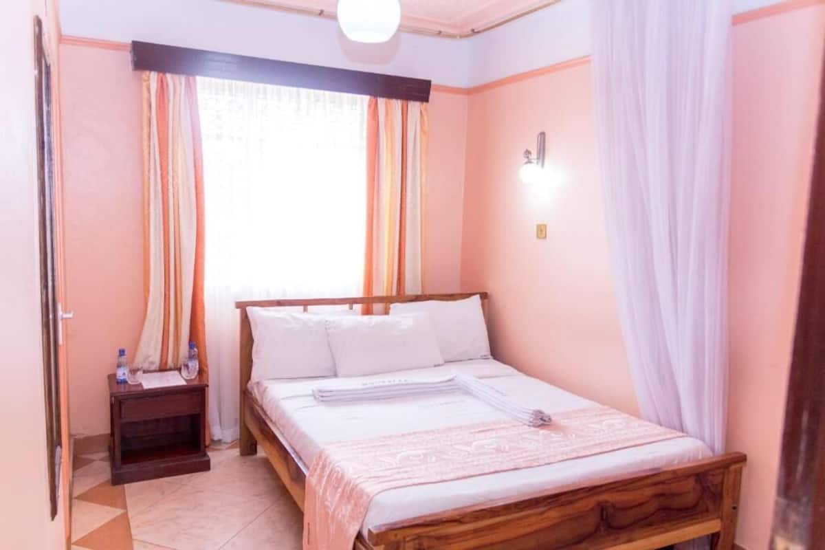 A bedroom with a wooden bed, a nightstand with water bottles, and a window with curtains.