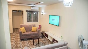 Een woonkamer met een bruine bank, een kleine tafel, een wit kastje en een televisie waarop 'beauty TV' staat.