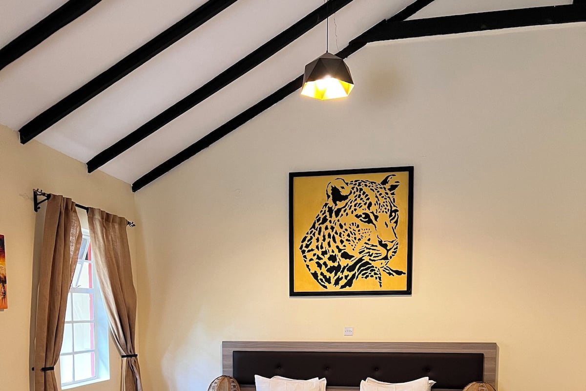 Un dormitorio con una cama, una silla, una obra de arte de un leopardo y una lámpara de techo.