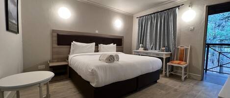 A modern hotel room with a large bed, bedside tables, a small desk, and a chair.