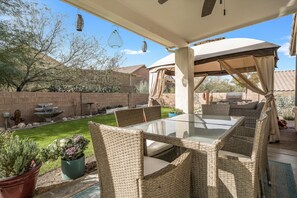 An outdoor patio with wicker furniture, a glass-top table, and a covered area with a canopy.