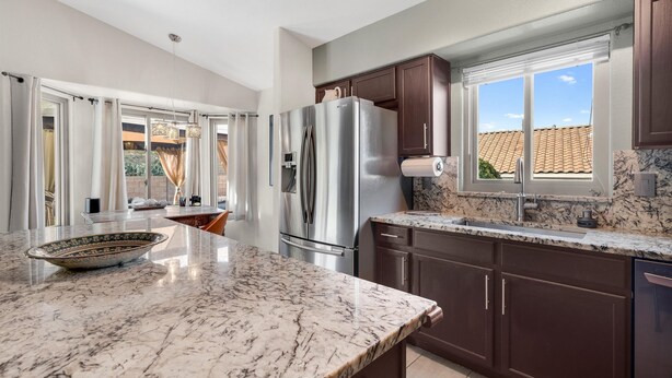 A modern kitchen with a large island, stainless steel appliances, dark wooden cabinets, and a view of the outside through a window. - Gorgeous backyard views- home gym- pet friendly! (Oro Valley)