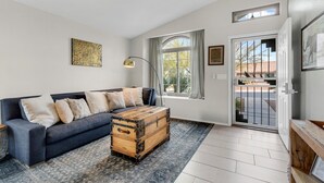 A living room with a dark blue sofa, a wooden trunk, a floor lamp, and a large window with curtains. - Gorgeous backyard views- home gym- pet friendly! (Oro Valley)