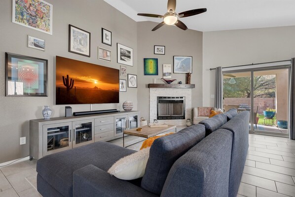 A modern living room with a large flat-screen TV, a fireplace, and a balcony with outdoor furniture.