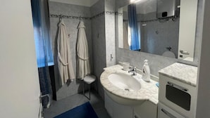 A modern bathroom with a large mirror, a sink, and a toilet. There are two towels hanging on hooks and a blue bath mat on the floor. - Saint Rita's (Torino)