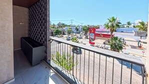 Un balcón con vistas a una calle, un autobús rojo y palmeras.