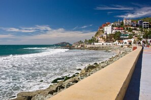 A coastal promenade with a rocky shoreline, a sandy walkway, and buildings with balconies overlooking the sea.