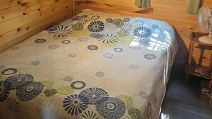 A wooden cabin room with a bed, a window with curtains, and a fan.