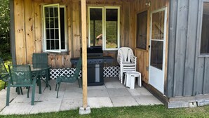 A wooden cabin with a covered porch, a grill, and outdoor seating.