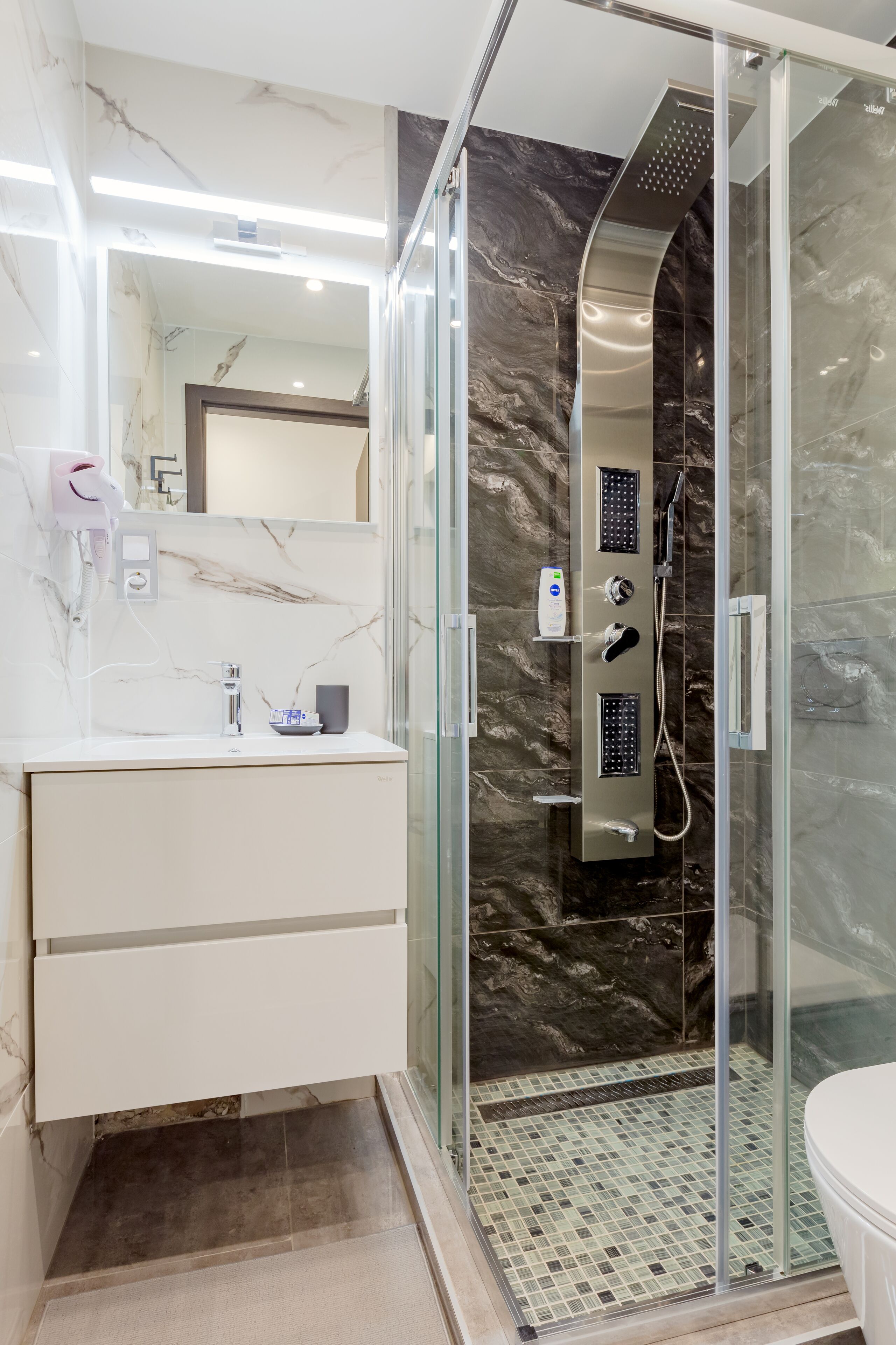 A modern bathroom with a glass-enclosed shower, a marble-tiled vanity, and a large mirror.